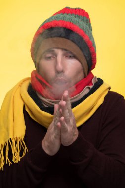 Sıcak giysili ve birkaç şapkalı bir adam soğukta kendini ısıtır ve ağzından buhar çıkar.