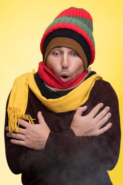 Sıcak giysili ve birkaç şapkalı bir adam soğukta kendini ısıtır ve ağzından buhar çıkar.