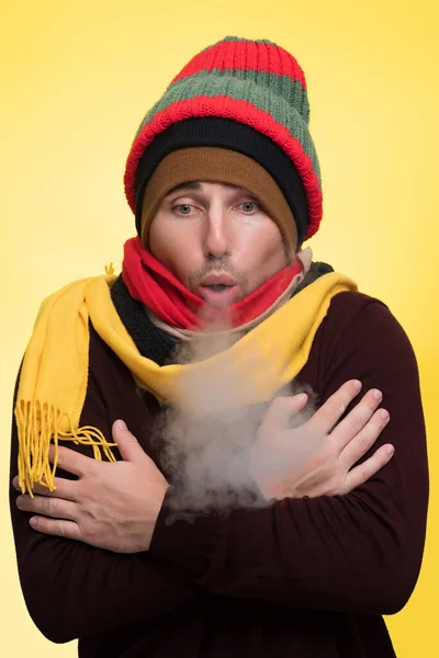 A man in warm clothes and several hats warms himself during the cold and steam comes from his mouth