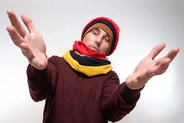 A man in colored warm clothes on a white background. He holds his arms outstretched towards the camera.