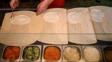İş yüzeyinde birkaç yaprak pita ekmeği ve çoktan hazırlanmış ve doğranmış sebzelerle dolu bir kase, aşçının elleri..