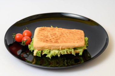 Siyah tabakta yeşil marullu panini, kiraz domatesli, hızlı ve lezzetli bir atıştırmalık..