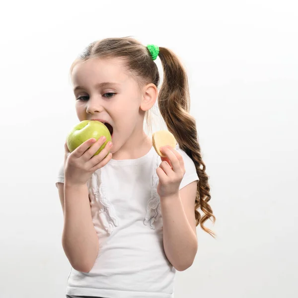 Green apple and potato chips, healthy and unhealthy food for children, little girl chooses apple over chips, child portrait on white background.
