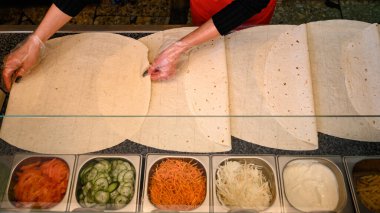 İş yüzeyinde birkaç yaprak pita ekmeği ve çoktan hazırlanmış ve doğranmış sebzelerle dolu bir kase, aşçının elleri..