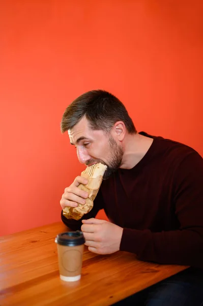 Homem Senta Restaurante Fast Food Morde Shawarma Contra Fundo Parede — Fotografia de Stock