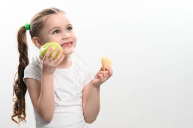 Yeşil elma ve patates cipsi, çocuklar için sağlıklı ve sağlıksız yiyecekler, küçük kız cips yerine elmayı seçer, beyaz arka planda çocuk portresi.