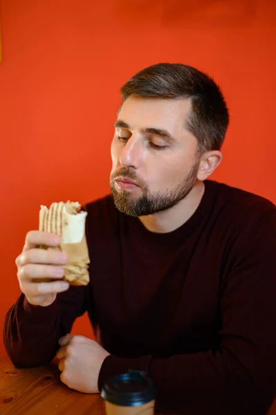 髭を生やした男が椅子に座ってシャワルマを食べ ファーストフードレストランでは迅速かつおいしい健康的な軽食を食べています — ストック写真
