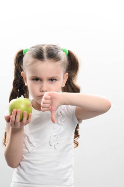 Beyaz arka planda küçük bir kızın portresi bir elinde bir elmayla diğerini işaret ediyor, kopyalama alanı ve sağlıklı beslenme.