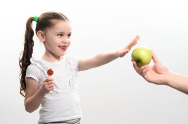 Küçük kız elma, şeker ve meyve yerine lolipop, sağlıklı ve sağlıksız yemek, beyaz geçmiş ve çocuk arasında seçim yapar..