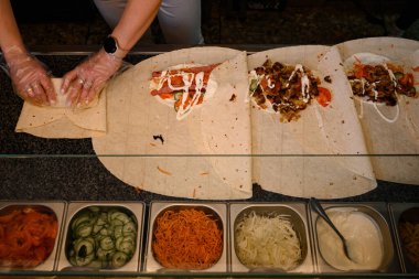 Tek kullanımlık eldiven giyen bir aşçı, bir fast food tesisi olan iş yüzeyinde shawarma çevirir..