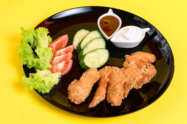 stock image Chicken nuggets with cucumber, tomatoes and lettuce on a black plate, chicken nuggets with mayonnaise and ketchup on a yellow background.