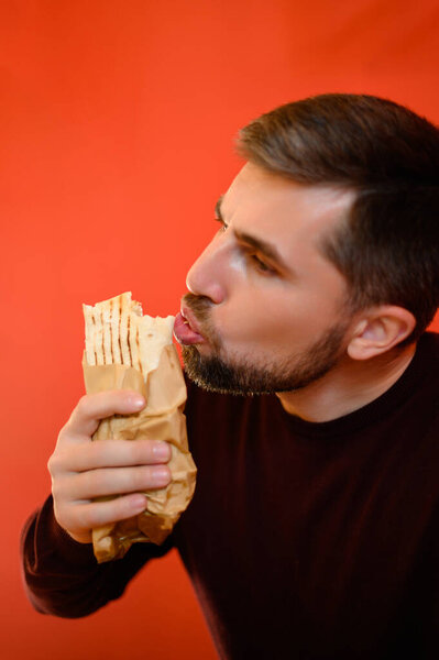 A man sits in a fast food restaurant and bites shawarma against a red wall background, shawarma for a quick snack.