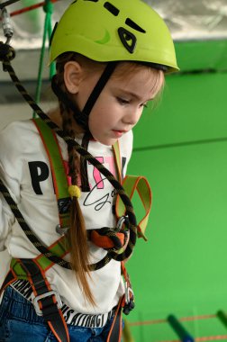 Küçük bir kız teleferik, miğfer ve emniyet kemeri takan teleferikli bir kızla kablo üzerinde yürüyor..