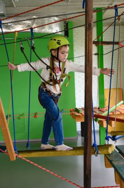 Küçük bir kız teleferik, miğfer ve emniyet kemeri takan teleferikli bir kızla kablo üzerinde yürüyor..