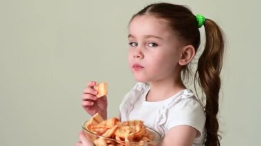 Bir kız kaseden domuz yağıyla cips alır ve yer, beyaz arka plan ve fotokopi alanında portre, sağlıksız ve sağlıksız yiyecekler..