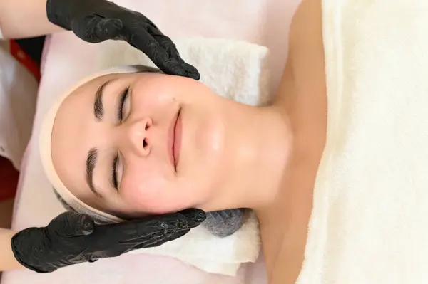 Portrait of a happy girl having a facial massage in a spa salon, relieving tension and giving her face freshness.
