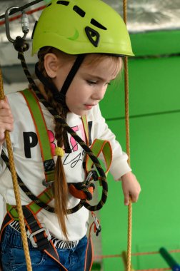 Küçük bir kız teleferik, miğfer ve emniyet kemeri takan teleferikli bir kızla kablo üzerinde yürüyor..