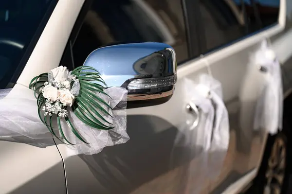 A white car in which the mirror and door handles are decorated with flowers, a car for weddings