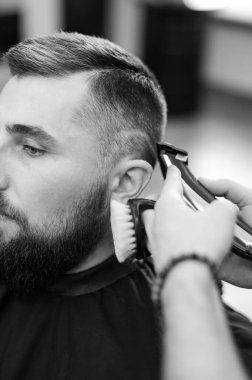 Berber, oval çizginin hatlarını müşterinin kafasında kırpıcı ile traş eder. Sakallı bir adam berber koltuğunda saçını kestirir..