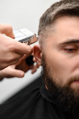 Berber, başındaki kısa saç kesimi sırasında şakağı kablosuz bir budayıcıyla tıraş eder..