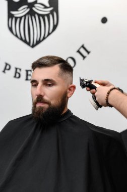 Bir berber berber dükkanında sakallı bir adamı keser. Kesici ile müşterinin kısa saç kesimi.