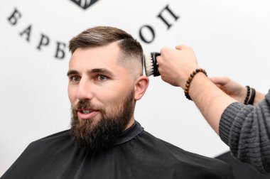 Berber, bir kuaförde müşterinin saçını keserken saçlarını tarar..