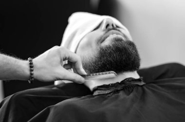 Berber, beyaz adamı keserken ve tıraş ederken tarakla sakal tarıyor.