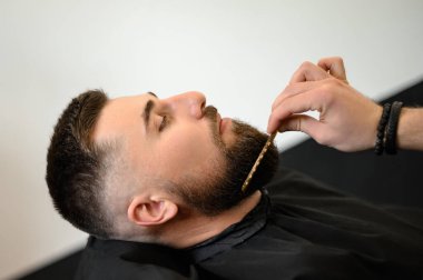 Berber, beyaz adamı keserken ve tıraş ederken tarakla sakal tarıyor.