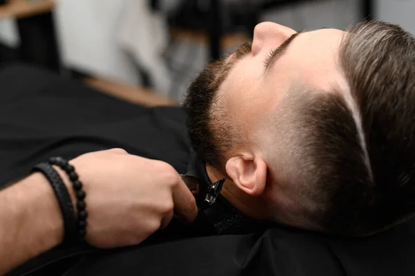 stock image Cutting a gentleman beard in a barbershop with a clipper. Shortening the length of the beard from the sides by the master for the client.