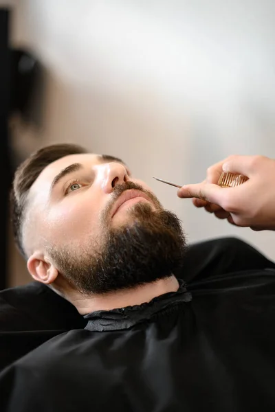 A barber stylist trims a Caucasian man mustache with scissors