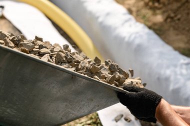 Drenaj alanı etrafındaki yeraltı sularının drenajı için çalışıyor. Bir adam el arabasından moloz döker yakın bir sipere..