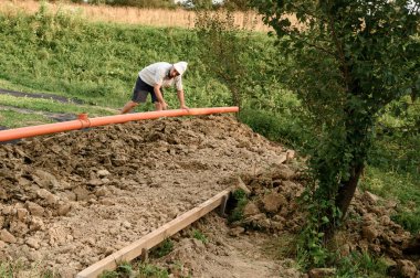 Tesisatçı bakım sırasında güçlendirilmiş turuncu kanalizasyon borusu yerleştirir..