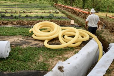 Yeraltı suyu drenajı sahada işe yarıyor. Bir işçi sarı delikli drenaj borusu taşır..