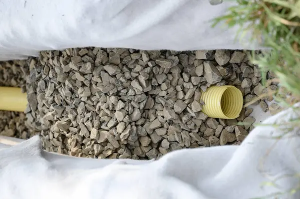 stock image Yellow corrugated pipe with perforation in a trench with crushed stone and geotextile. Drainage works for the removal of ground water in the field.