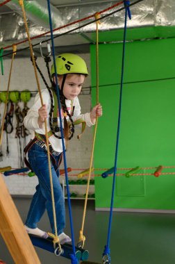 Küçük bir kız teleferik, miğfer ve emniyet kemeri takan teleferikli bir kızla kablo üzerinde yürüyor..