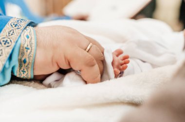Rahip, çocuğun vaftiz ayinini gerçekleştirir ve bacağını kutsal mira ile kutsar. Hristiyan vaftiz ayini..