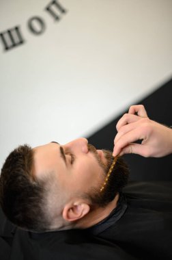 Berber, beyaz adamı keserken ve tıraş ederken tarakla sakal tarıyor.