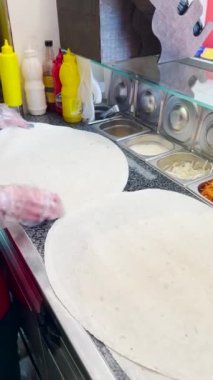 İş yüzeyinde birkaç yaprak pita ekmeği ve çoktan hazırlanmış ve doğranmış sebzelerle dolu bir kase, aşçının elleri..
