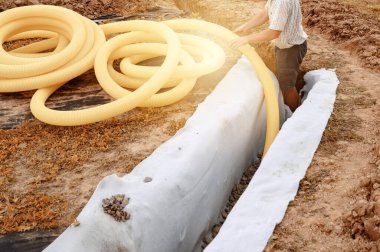 Yeraltı suyu drenajı sahada işe yarıyor. Bir işçi sarı delikli drenaj borusu taşır..