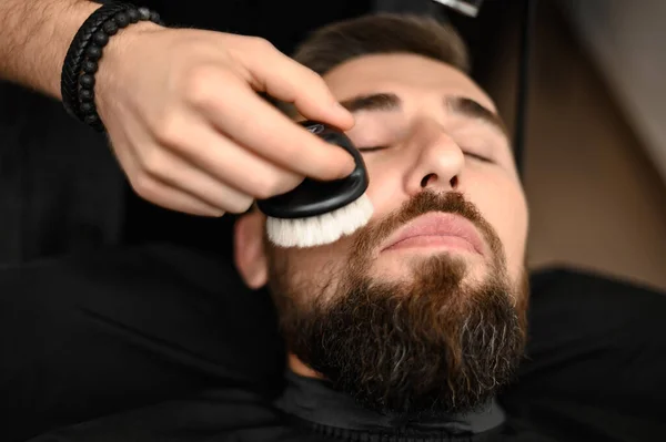 Barber sweeps hair with a brush while cutting a clients hair in a salon.