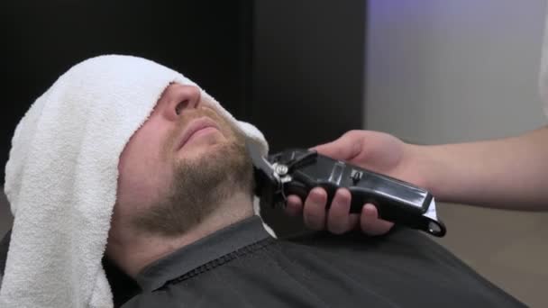クライアントの頭はひげのトリム中にタオルで覆われています クライアント4Kビデオのマスターによる側面からのひげの長さを短縮する — ストック動画