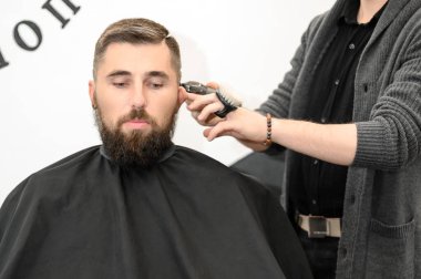 Bir berber berber dükkanında sakallı bir adamı keser. Kesici ile müşterinin kısa saç kesimi.