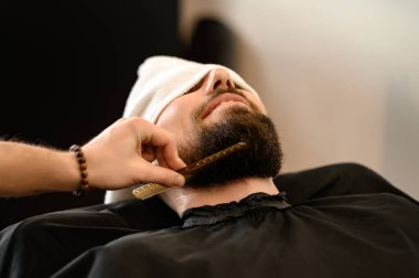 Berber, beyaz adamı keserken ve tıraş ederken tarakla sakal tarıyor.