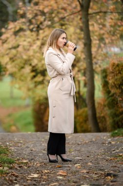 Sonbahar parkında genç bir kız kahve içer, parkta dinlenir..