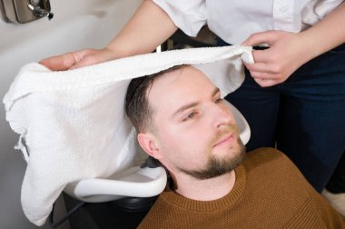 Bir kuaför berber dükkanında yıkandıktan sonra bir müşterinin kafasını beyaz havluyla siler..