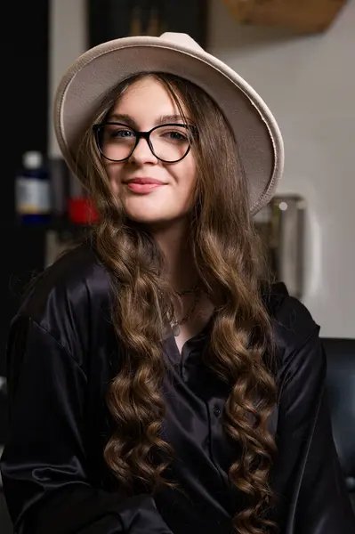 A female student is sitting in the classroom during a break between pairs. Portrait of a young girl in a hat and with long hair.