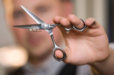 İvano-Frankivsk, Ukrayna, 23 Şubat 2024: Bir erkek berber arka planda berberin yüzü olan sonsuz salıncak markasının makasını tutuyor..