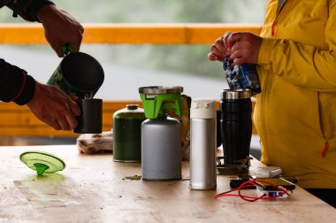 Turistler, ahşap bir masadaki bir turist barınağında gaz tüpleriyle kahve yapıyorlar..