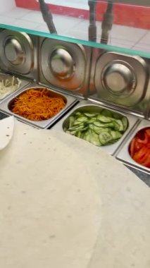 İş yüzeyinde birkaç yaprak pita ekmeği ve çoktan hazırlanmış ve doğranmış sebzelerle dolu bir kase, aşçının elleri..