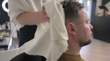 Bir kuaför, bir berber dükkanında 4K videoda yıkandıktan sonra bir müşterinin kafasını beyaz havluyla siler..